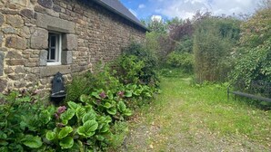 A stone building with a window and a small garden area with various plants. - Charming eco-gîte, no TV or internet, pets welcome (La Mouche)