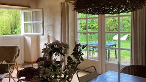 A room with a wooden ceiling, a large window with a view of greenery, a table, and two chairs. - Charming eco-gîte, no TV or internet, pets welcome (La Mouche)
