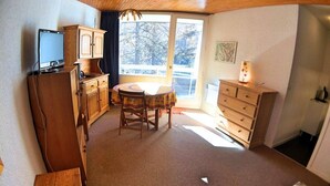 Una habitación compacta con un armario de madera, una pequeña mesa con sillas, un aparador y un televisor sobre un mueble.