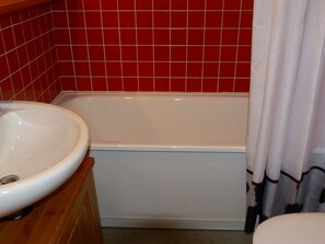 Un baño con un lavamanos blanco, una bañera y una pared de azulejos rojos.