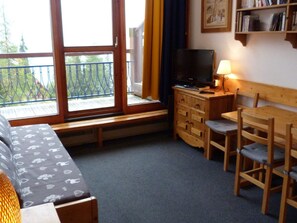 Una habitación acogedora con un sofá, una mesa de madera con sillas, un televisor y una estantería.