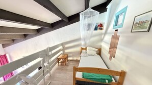 A small, cozy room with a wooden bed, a small table, and a white chair. - Spacious Apartment with Mezzanine and Parking, Near the Beach (Argelès-sur-Mer)