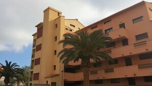 A multi-story building with a flat roof, balconies, and a palm tree in front. - Spacious Apartment with Mezzanine and Parking, Near the Beach (Argelès-sur-Mer)