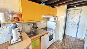 A compact kitchen with yellow cabinets, a microwave, a stove, and a sink. - Spacious Apartment with Mezzanine and Parking, Near the Beach (Argelès-sur-Mer)