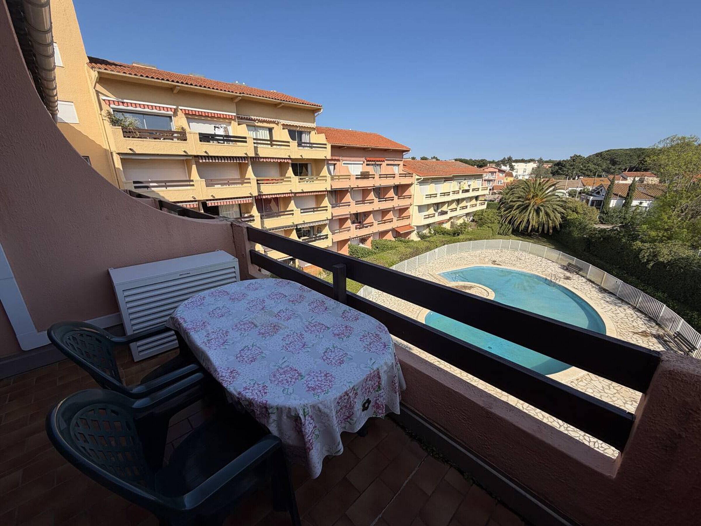 Un balcon avec une table et des chaises, une piscine et une vue sur des immeubles d’habitation.