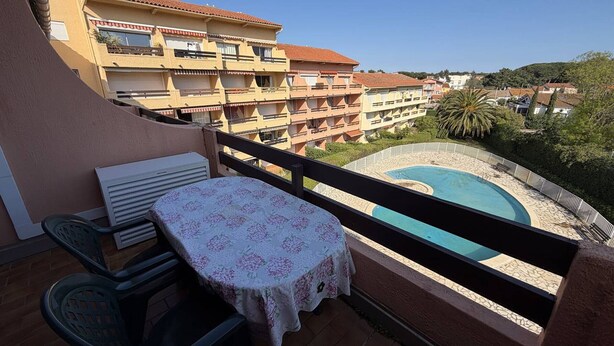 A balcony with a table and chairs, a pool, and a view of apartment buildings. - Spacious Apartment with Mezzanine and Parking, Near the Beach (Argelès-sur-Mer)