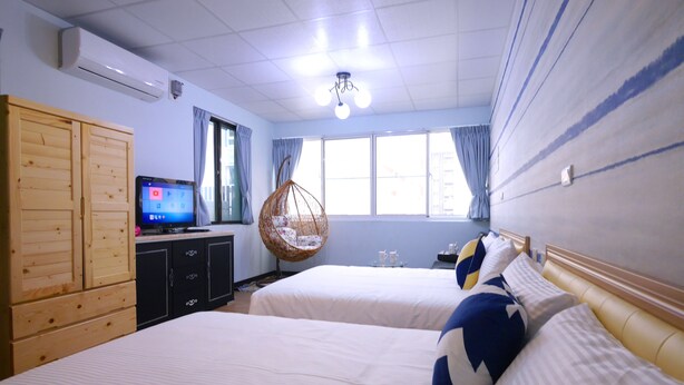 Habitación de hotel con dos camas, televisión, sillón colgante y un amplio ventanal.