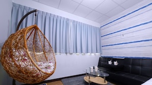 Una habitación moderna con una silla colgante, un sofá negro, una mesita de centro de vidrio y una pequeña mesita auxiliar.