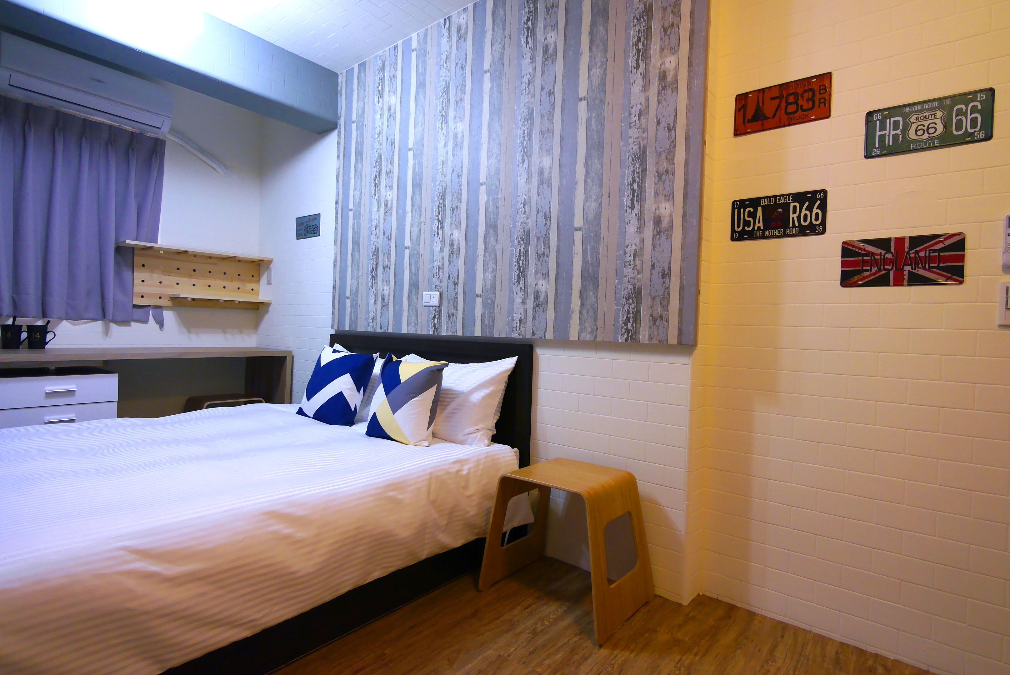 A bedroom with a bed, a wooden stool, a wall-mounted shelf, and decorative license plates.