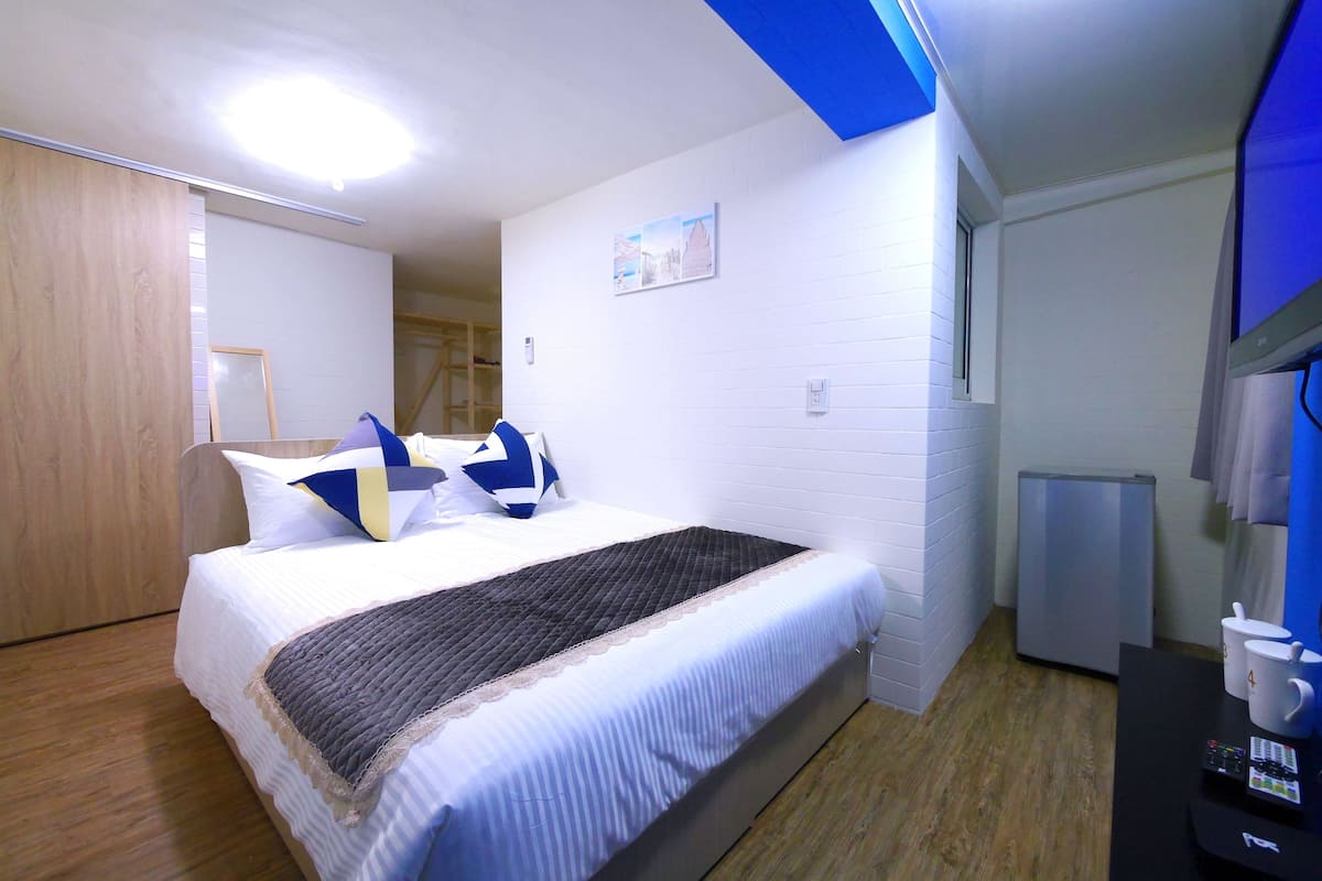 A neatly arranged bedroom with a bed, a small desk, and a refrigerator.