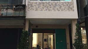 Un edificio de varios pisos con fachada de tejas, una puerta verde y un letrero que indica prohibido estacionar.