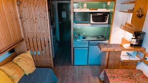 Une pièce de taille modeste comprenant un lit, un petit coin cuisine et une cloison en bois.