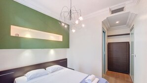 A modern hotel room with a large bed, a wall-mounted light fixture, and a door leading to another room.