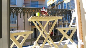 A balcony with a yellow table and two chairs, a bottle of wine, and two glasses.