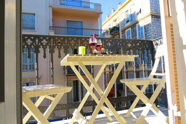 A balcony with a yellow table and two chairs, a bottle of wine, and two glasses.