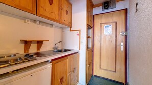 Een kleine keuken met houten kastjes, een wastafel en een kleine koelkast.