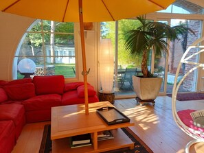 A cozy living room with a red sofa, a wooden coffee table, and a large window with a view of a garden. - Homerez - House near Montluçon (Montluçon)