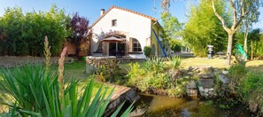 A house with a stone water feature, a garden with various plants, and a small pond. - Homerez - House near Montluçon (Montluçon)