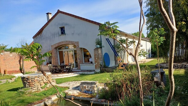 A house with a stone foundation, a small pond, and a patio with outdoor furniture. - Homerez - House near Montluçon (Montluçon)