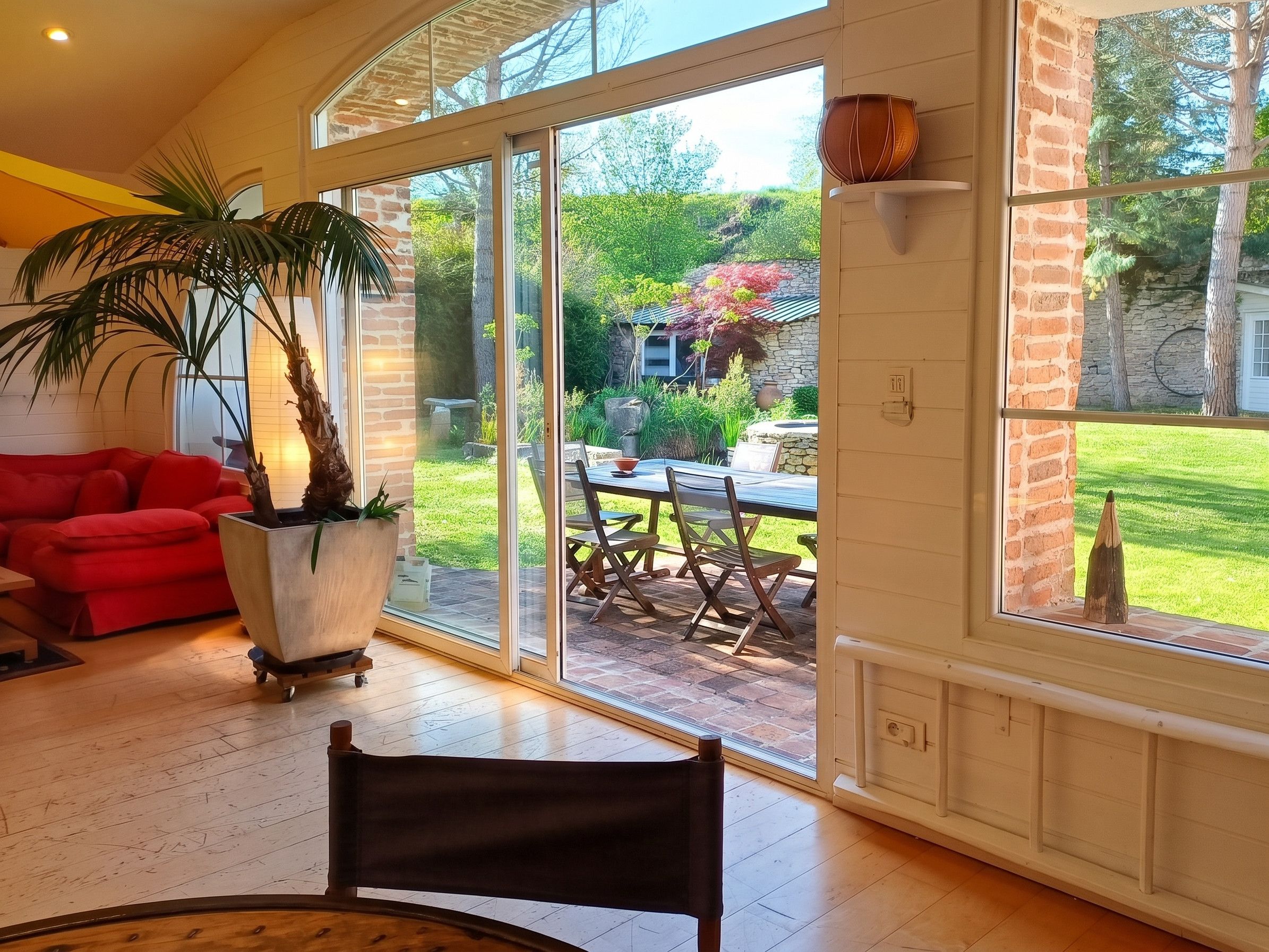 A spacious living area with a sliding glass door leading to a patio, a red sofa, a large potted plant, and a dining table with chairs.