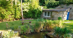 A stone cottage with a bench, surrounded by lush greenery and a small pond. - Homerez - House near Montluçon (Montluçon)