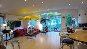 A spacious living area with a red sofa, a hanging chair, a wooden dining table, and a large window offering a view of the outdoors. - Homerez - House near Montluçon (Montluçon)