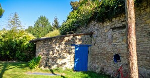 A stone building with a blue door, surrounded by greenery and trees. - Homerez - House near Montluçon (Montluçon)