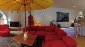 A modern living room with a red sectional sofa, a wooden coffee table, and a yellow umbrella. There is a fireplace, a violin, and a painting on the wall. - Homerez - House near Montluçon (Montluçon)