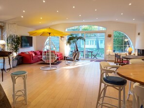Een ruime woonkamer met een rode bank, een witte schommelstoel en een eettafel met stoelen.
