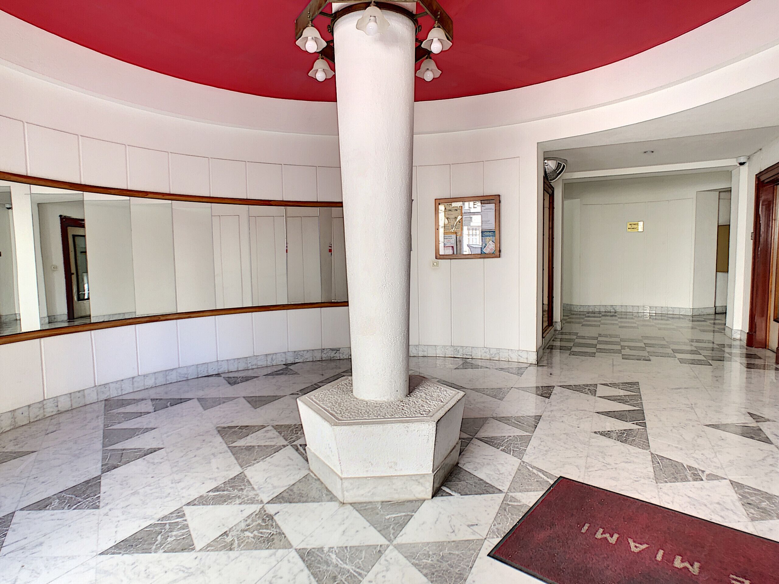 A spacious lobby with a high ceiling, a central column, and a checkered marble floor.