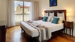 Habitación de hotel con una cama grande, piso de madera, ventana con cortinas y una obra de arte colgada en la pared.