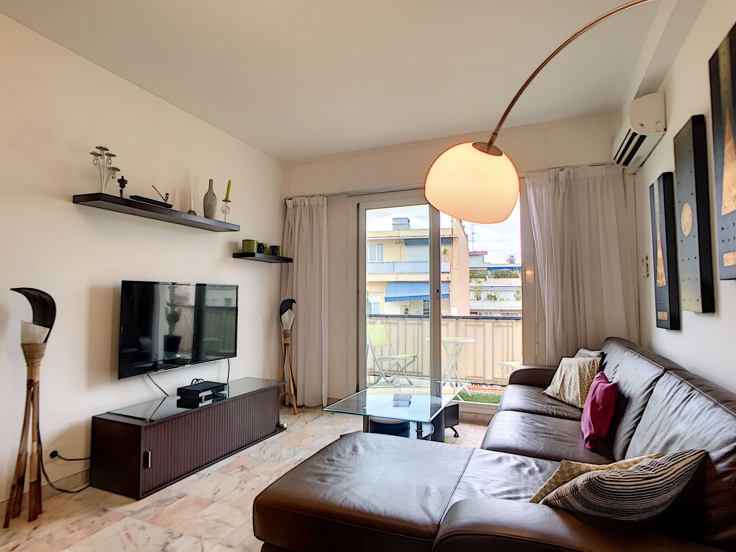 A modern living room with a leather sofa, a flat-screen TV, a glass coffee table, and a pendant light.