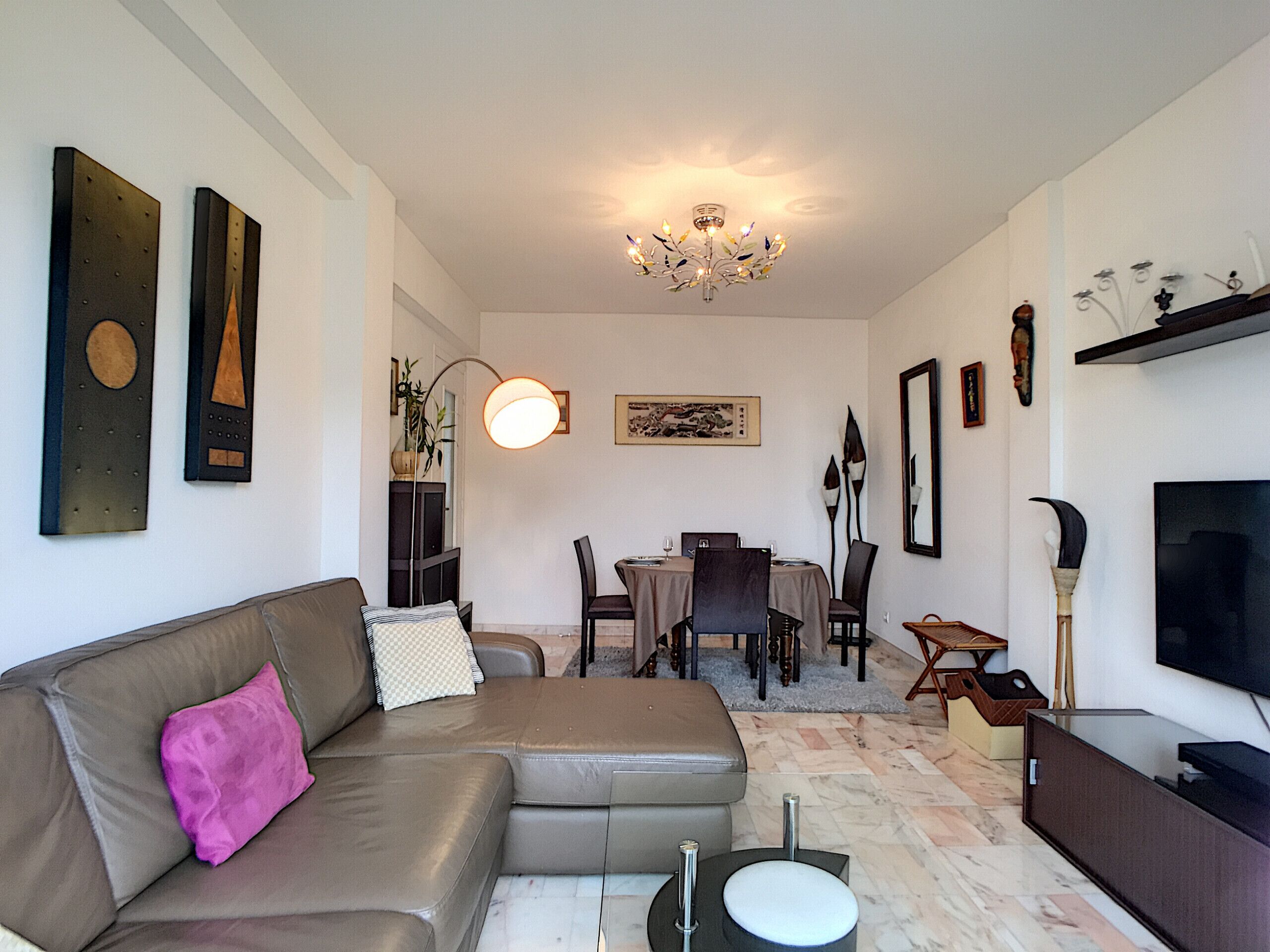 Una sala de estar moderna con sofá, una mesa de comedor, sillas, televisor y una lámpara de araña.