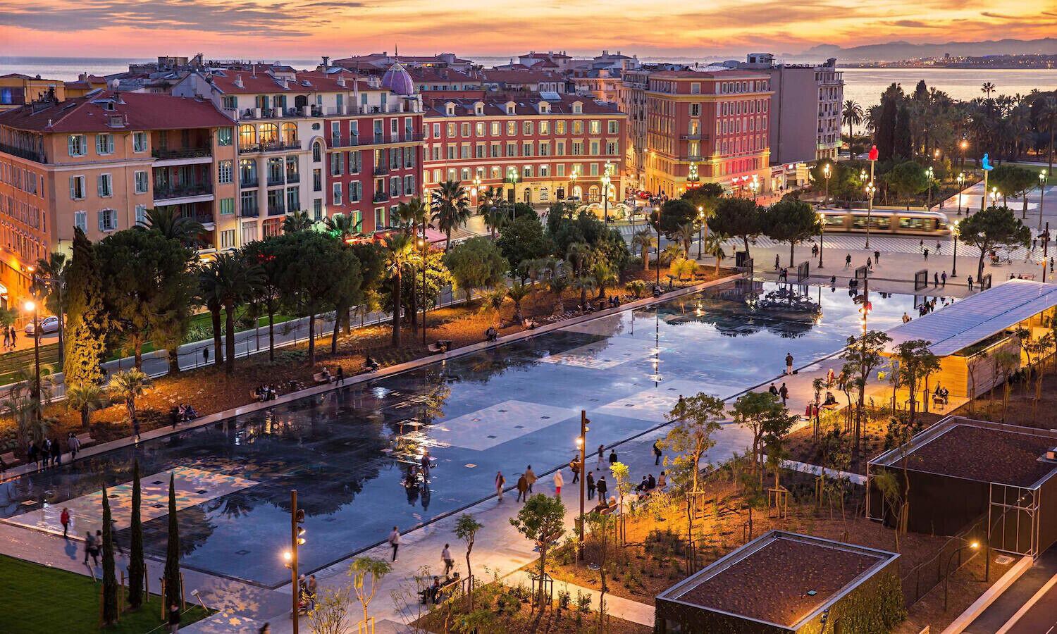 A cityscape with a large reflective water feature, surrounded by buildings and palm trees.