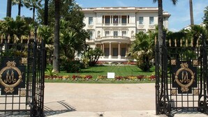 Un edificio imponente con una entrada formal, palmeras y un jardín bien cuidado.