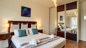 Una habitación de hotel ordenada con una cama grande, lámparas de noche, un espejo y un cuadro en la pared.