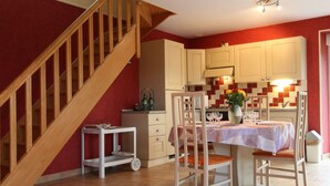 Un comedor con una escalera de madera, una pequeña mesa con sillas y una cocina al fondo.