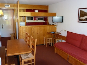 A compact room with a wooden dining table, chairs, a red sofa, a television, and a kitchenette with a microwave and a refrigerator. - 4-bedroom duplex, ski-in/ski-out, near shops, balcony, 8-10 pers, Les Arcs 1800 (Les Arcs 1800)