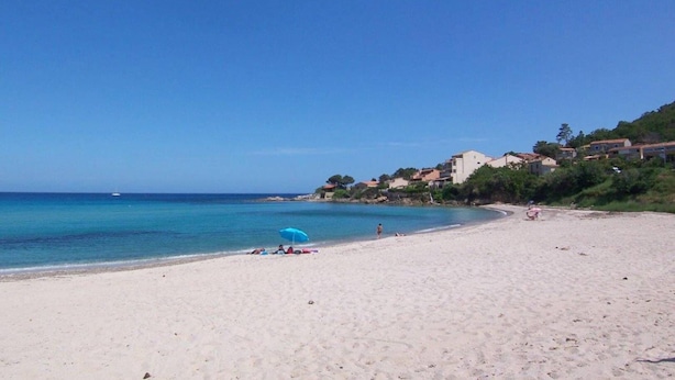 A beach with clear blue water, a few people, and buildings in the background.