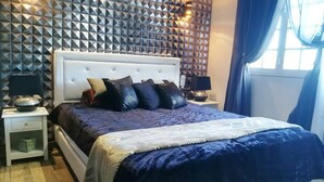 A bedroom with a tufted headboard, a patterned bedspread, and a geometric wall design.