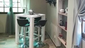 A dining area with a round table and two chairs, a TV mounted on the wall, and a shelf with decorative items.