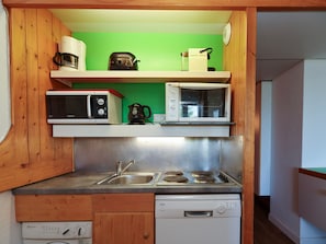 A compact kitchen with a microwave, toaster, and coffee maker on shelves, a sink, stove, and dishwasher below.