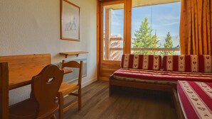 A room with a wooden bed, a wooden chair, a small table, and a large window with curtains. - Ski-in/ski-out studio, balcony, pets allowed, Arc 1800 (Les Arcs 1800)