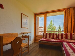 A room with a wooden bed, a wooden chair, a small table, and a large window with curtains.