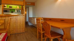 A wooden dining area with a table and chairs, a kitchen with green backsplash, and a wall-mounted light fixture. - Ski-in/ski-out studio, balcony, pets allowed, Arc 1800 (Les Arcs 1800)