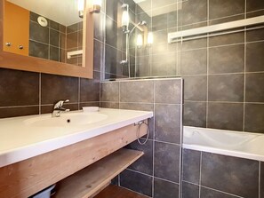 A bathroom with a wooden vanity, a sink, a mirror, a bathtub, and a towel rack. - Renovated apartment for 8, ski-in/ski-out with parking (Les Menuires)