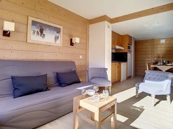 A cozy living room with a sofa, two armchairs, a small wooden table with glasses, and a kitchen area with a refrigerator and microwave. - Renovated apartment for 8, ski-in/ski-out with parking (Les Menuires)