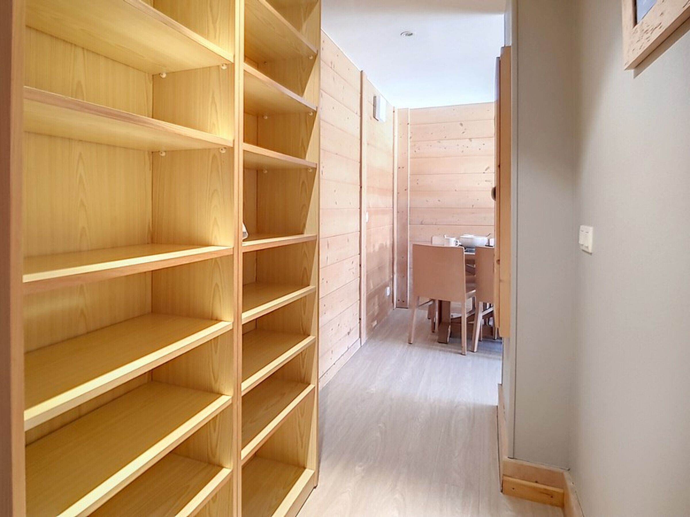 A room with wooden shelving units and a dining area with chairs and a table.