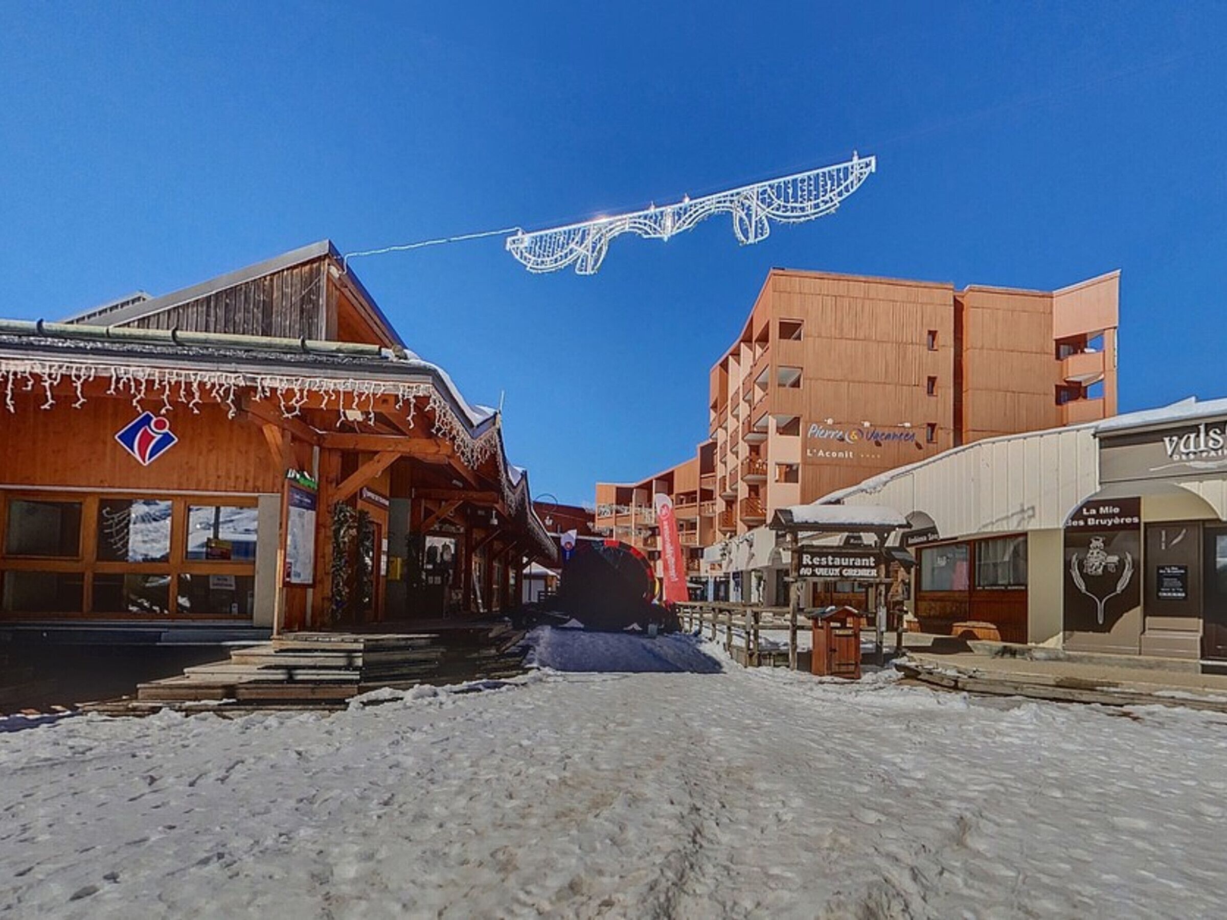 A snowy street with wooden buildings, including a restaurant and a hotel.