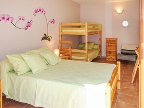 Una camera con un letto a castello, una coperta verde, un comò in legno e una lampada fissata al muro.